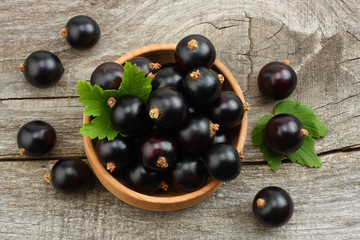 black currant in wooden bowl with green leaf on old wooden background. top view