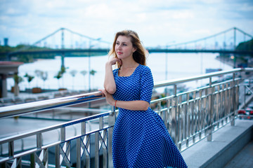 A young blond girl of European appearance walk  in the city, wearing a blue polka dot dress. Vintage style in the modern world