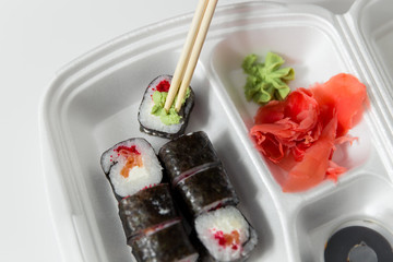 Hand takes roll. Set with chopsticks, ginger, soy sauce in container delivery.