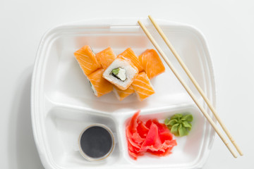 roll with chopsticks, rolls, sushi. chopsticks, ginger, soy sauce in container delivery on white background