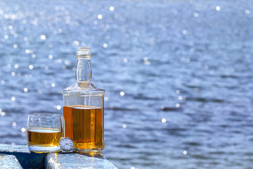 Bottle and glass of the whiskey with watches by the lake