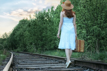 Obraz premium girl in a white sundress and wicker suitcase walking on rails
