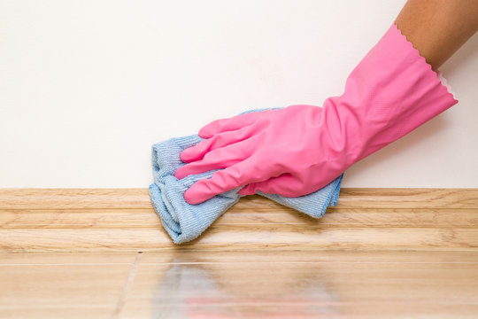Hand in rubber protective glove cleaning baseboard on the floor from dust with rag at the wall. Early spring cleaning or regular clean up. Maid cleans house.