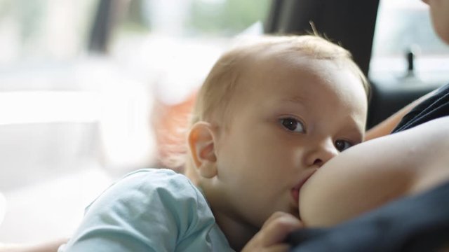 Anonymous woman giving breast to a newborn baby sitting in the car. Close-up
