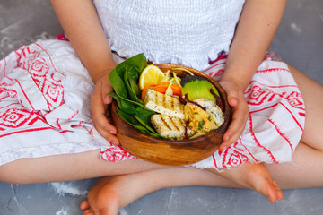 Buddha bowl with grilled tofu and vegetables in the child's hands. Child vegan concept.