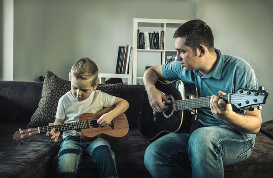 Father teaching his son to play on guitar at home. Son play on u