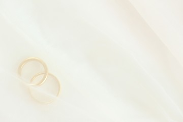 Closeup of two golden wedding rings under white wedding veil