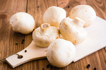 Whole fresh champignons on cutting board on wooden table