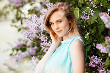 Fototapeta premium Blonde girl with bouquet of wild flowers outdoors A model in a turquoise dress against a background of a lilac bush.