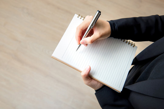Woman writing on empty notebook with pen