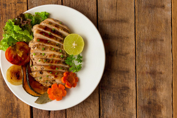 Sliced chicken breast barbecue on white plate served with grilled vegetable. Delicious  chicken breast steak and salad for dinner. Homemade chicken breast barbecue on wood table for background.