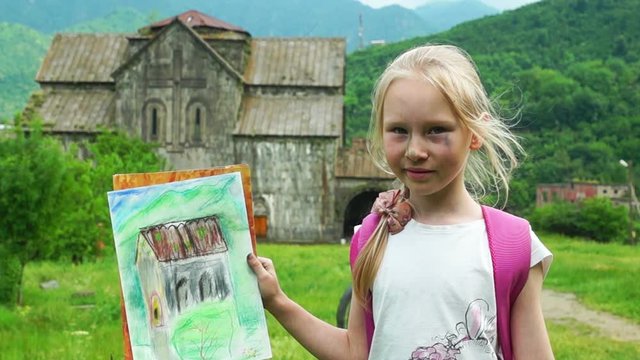 Schoolgirl showing her drawing standing near ancient church in armenian monastery Akhtala