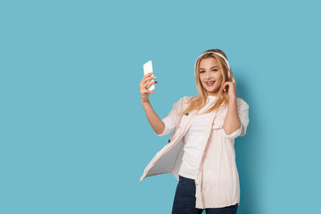 Cheerful blonde girl with smartphone smiling and listening to the music