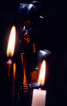 dark close-up image of an african statue with two burning candels