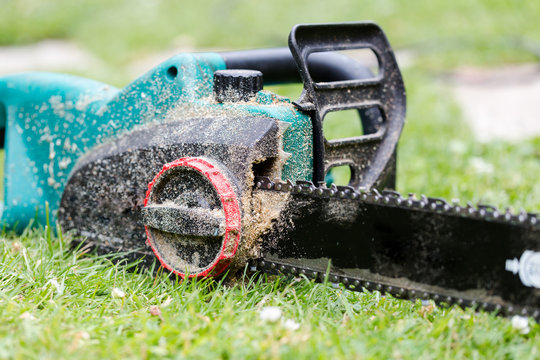 Dirty in sawdust chain saw on grass in garden close up