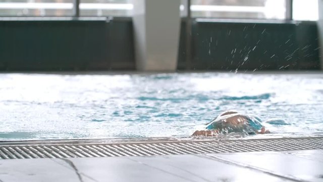  Medium shot with slow motion of beautiful woman in swimsuit diving into swimming pool with clean blue water, then emerging from the pool and smiling for camera 