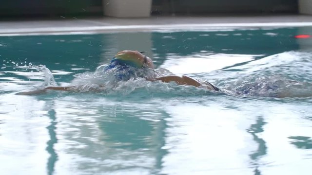 Slow motion tracking of female athlete in cap and goggles swimming in pool with front crawl technique 