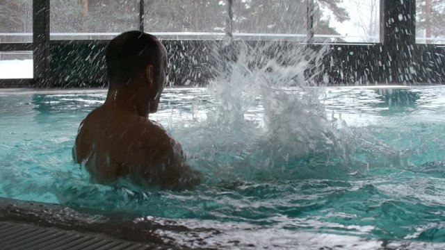 Slow motion of happy young woman in swimsuit jumping into blue water of indoor swimming pool, then playing and dunking muscular man 