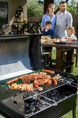 family spend time together at barbecue. Selective focus of meat and vegetables cooking on grill