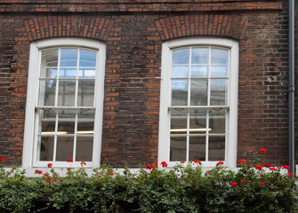 Fototapeta na wymiar White Windows in Old Brick Wall Over Flower Boxes