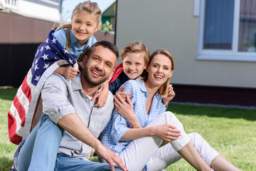 Happy family with american flag hugging outdoors, Independence Day concept
