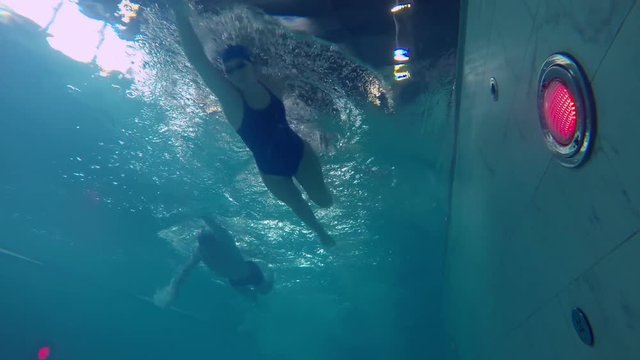 Underwater shot of male and female competitive swimmers in swimwear racing with front crawl stroke in pool with clear water