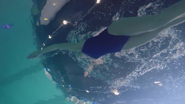 Underwater PAN of female competitive swimmer in cap and goggles swimming with front crawl stroke in pool with clear water