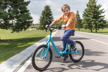 smiling casual kid boy riding bicycle in park at daytime