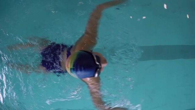 Top view tracking of female athlete in cap and goggles swimming in pool with breaststroke 