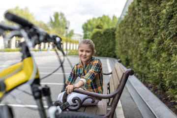 smiling pre-adolescent girl looking at camera while sitting on bench at park