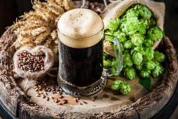 Dark beer with foam, wheat and hops on oak barrel