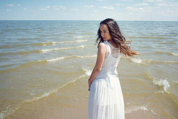 Fototapeta na wymiar Young beautiful brunette woman in white dress on the seashore. Back view