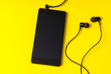 Mobile phone with headphones on yellow background