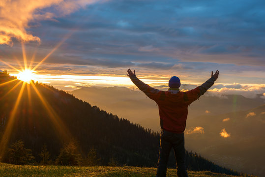 Man traveler with open arms admires a colorful sunset in the mountains