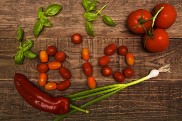 Vegetables on a wooden table, tomatoes of different varieties, basil, red long pepper and fresh green onions. Vegetables beautifully harmoniously spread out on a wooden background in word BIO