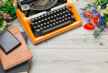 Orange vintage typewriter with a bouquet of summer field flowers on a gray background.