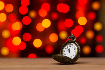 Closeup vintage old clock in the bokeh on brown wood background. The clock is near midnight. Concept Christmas and happy new year or everything related to time.