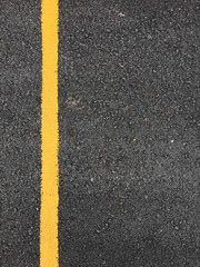 Fototapeta premium Yellow paint line on black asphalt road surface texture. space transportation background