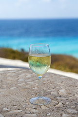 A glass of white wine against a turquoise sea. Beautiful place for having a drink on a hot day.