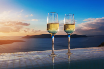 Two champagne glasses on the edge of infinity swimming pool at sunset on Santorini island