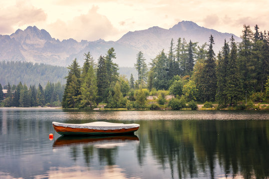 Beautiful alpine lake surrounded by rocky mountains with boat and green fir trees, popular tourist destination, lake Strbske pleso, High Tatras, Slovakia (Slovensko)