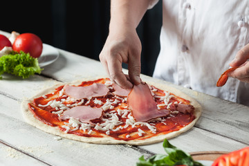 Closeup hand of chef baker in white uniform making pizza at kitchen