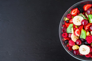 Tasty fresh fruit salad in glass plate on dark background. Salad with summer berries. Flat lay, top view