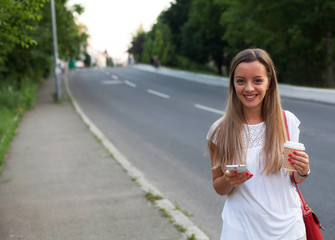 Young woman with a coffee to go and phone standing at the street