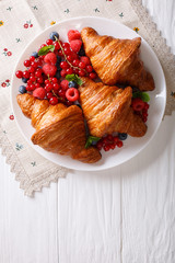 Freshly baked croissants with raspberries, blueberries and currants close-up. Vertical top view