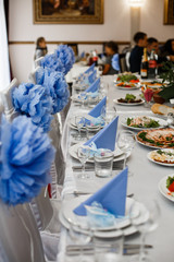 Triangles of blue napkins stand on white plates on dinner table