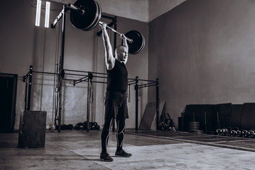 Black and white full length portrait of Strong man lifting a barbell during crossfit workout at gym
