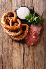 German appetizer: sliced salami and pretzels with sauce close-up on the table. Vertical top view