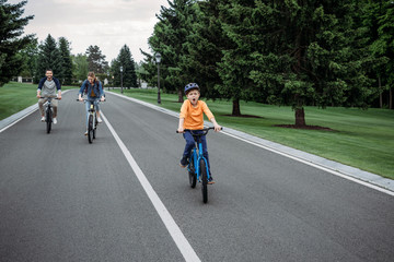 little boy riding bicycle with his parents behind on asphalt road