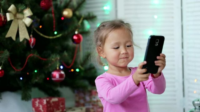 Little cute girl making selfie with Christmas tree on the background